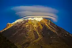 Une montagne arrondie avec un peu de neige au sommet et de nuages en forme d'anneau ou de couronne.