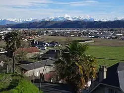 Photographie en couleurs d'une ville et de champs, avec en fond des montagnes.