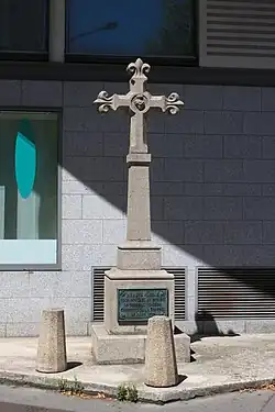 Photo en couleur d'une croix commémorative en pierre au pied d'un bâtiment.