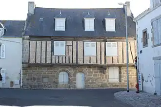 Vue d'une façade de maison en granit, pans de bois et toit d’ardoise.