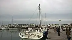 Vu de l'arrière, dans un port, sans les voiles, bateau au mât remplacé par la bôme cassée en deux et réassemblée durant la course.