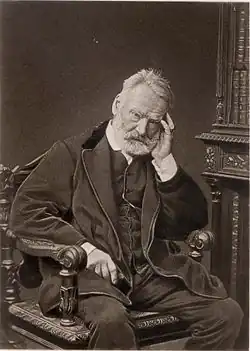 Portrait photographique d'un homme assis sur un fauteuil la main gauche appuyée sur la tempe.