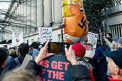personnes dans une manifestation avec des pancartes dont une personne avec un ballon gonflable de Trump avec une croix gammée sur le ventre