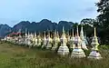 Tombes blanches et dorées en enfilade dans un cimetière bouddhiste au lever du soleil, avec les montagnes karstiques de Vang Vieng.