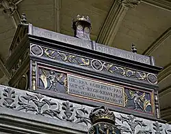 Photo d'un coffre oblong de couleur sombre décoré de motifs dorés, avec des inscriptions en latin. Il est surmonté d'une couronne.