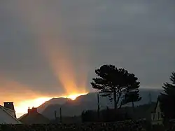 Sur un fond nuageux un rayon de Soleil perce au-dessus d'une montagne.