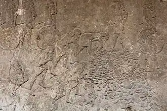 Des ouvriers transportent des pierres extraites de la carrière et les jettent en tas, sous la surveillance de soldats.