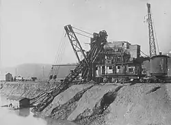 Photo ancienne en noir et blanc montrant une excavatrice devant un point d'eau.