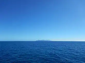Étendue d'un océan, et une île en son centre au loin.
