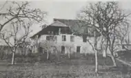 Photo noir et blanc d'une grande demeure située dans un verger avec des arbres sans feuilles.