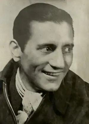 Photographie en noir et blanc du visage d'un homme. Il sourit et regarde vers sa gauche.